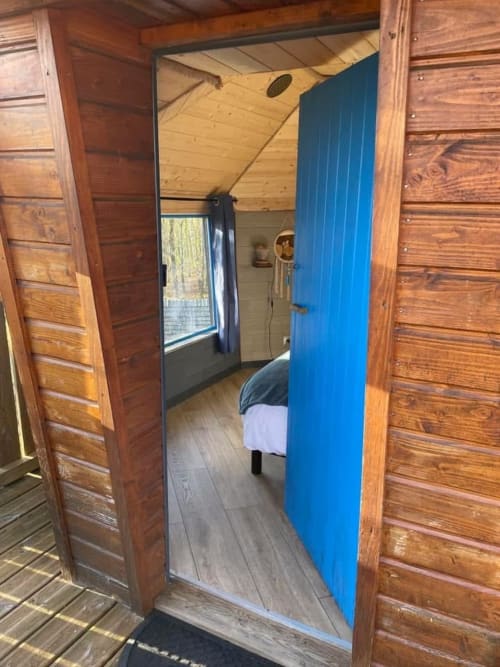Cozy wooden cabin bedroom with blue partition at Les Murmures du Bois, featuring bed and garden view window