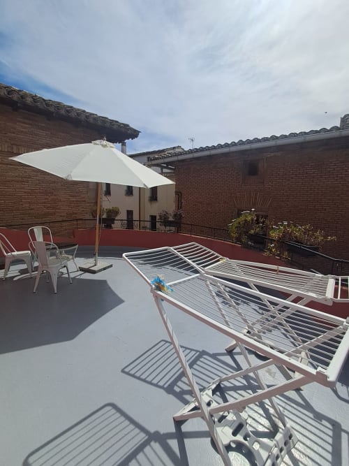 Terraza en la azotea del hostal Casa Arqueña en Los Arcos con tumbonas, sombrilla blanca y edificios de ladrillo