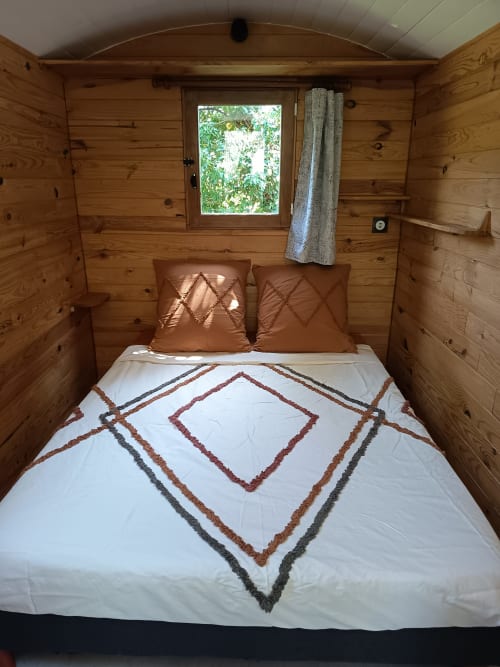 Chambre chaleureuse en bois à La Roulotte de Maison Maliga avec parure décorée et vue sur le jardin