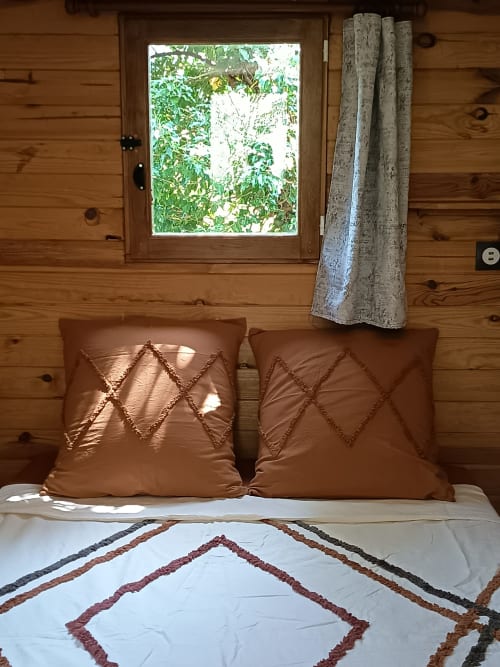 Chambre cosy de La Roulotte à la Maison Maliga B&B avec coussins marron, literie motifs et vue sur le jardin