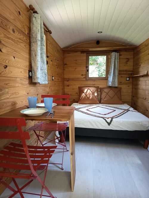 Intérieur cosy d'une roulotte en bois à Maison Maliga avec lit, coin repas et vue sur le jardin en France