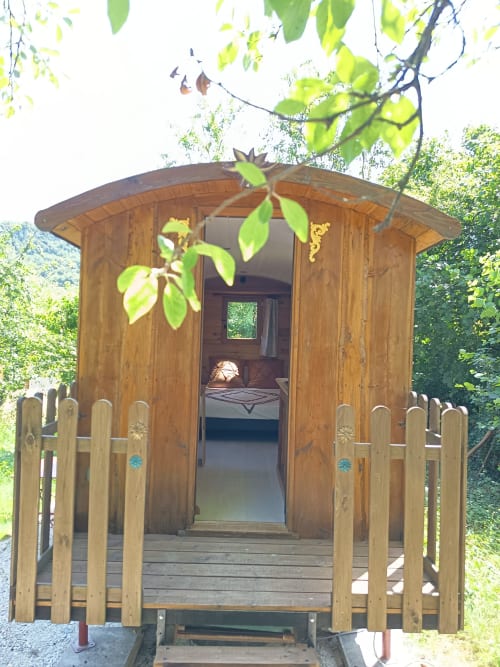 Roulotte de glamping en bois avec porte ouverte à Maison Maliga à Saint-Pierre-de-Curtille, entourée de verdure