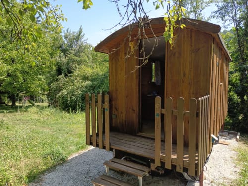 Roulotte rustique en bois avec terrasse entourée de verdure luxuriante à Maison Maliga à Saint-Pierre-de-Curtille