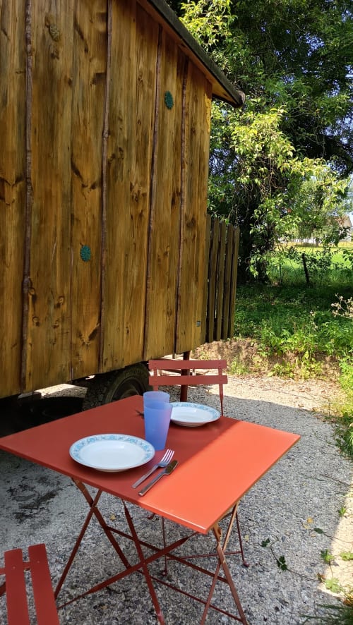 Espace de repas en plein air à La Roulotte, Maison Maliga, avec table et chaises rouges devant une structure en bois
