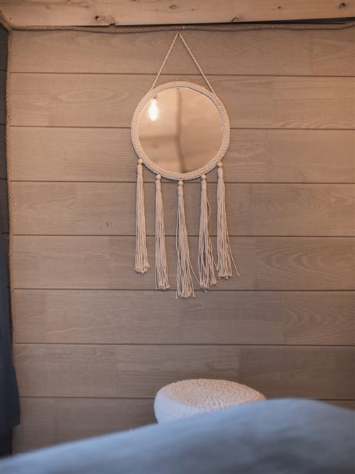 Boho macramé mirror with tassel fringe hanging on wooden wall in Nuit céleste bedroom at Les Murmures du Bois B&B