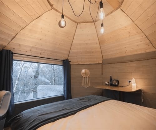 Cozy wooden dome room at Les Murmures du Bois with bed, pendant lights, and snowy forest view through large window