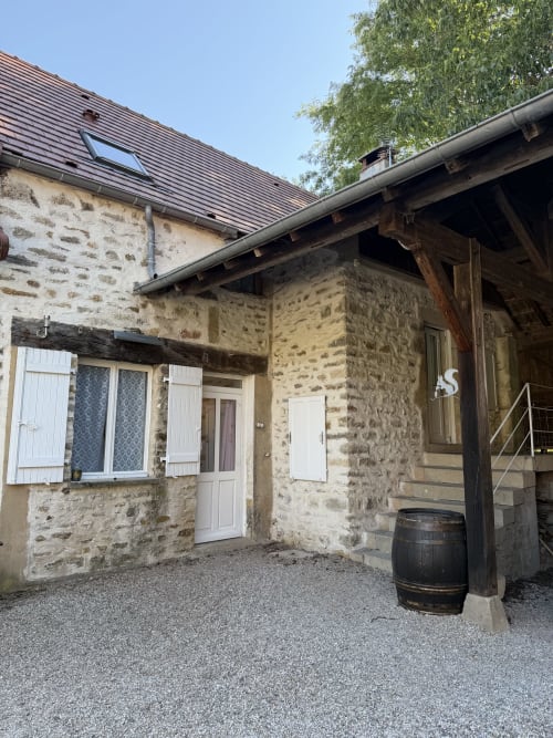 Charmante maison en pierre avec toit sombre au Domaine les Bertrands à Couches, volets blancs et poutres en bois rustique.