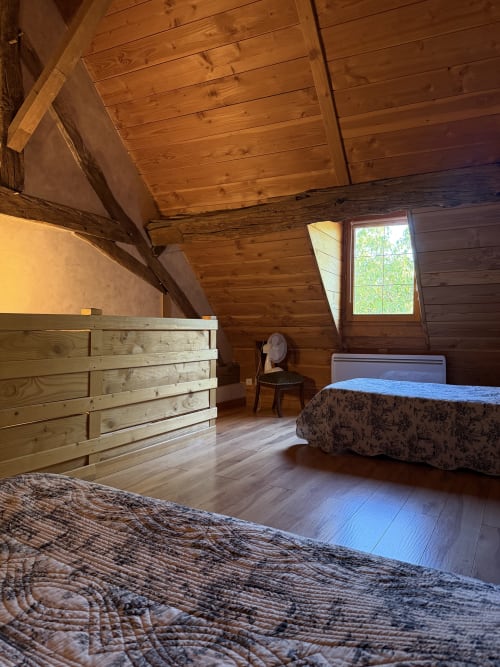 Cozy wooden cottage bedroom at Domaine les Bertrands with two beds, wooden beams, and garden view window