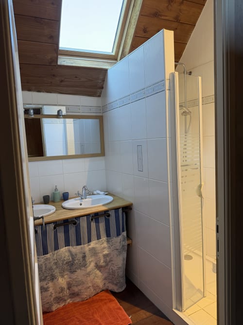 Modern bathroom in Domaine les Bertrands cottage with double sink, shower, skylight, and wooden ceiling.
