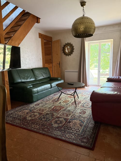 Spacious cottage living room at Domaine les Bertrands with green leather sofa, fireplace, and garden views