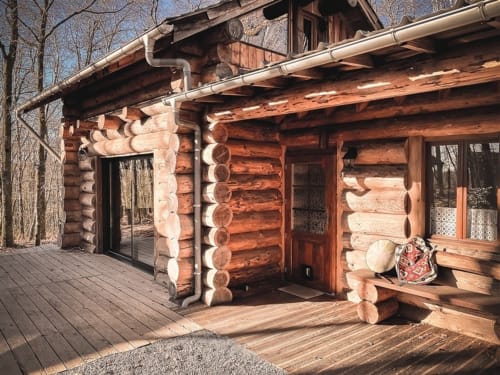 Rustic log cabin exterior at Les Murmures du Bois with wooden deck, large windows, and forest views in France