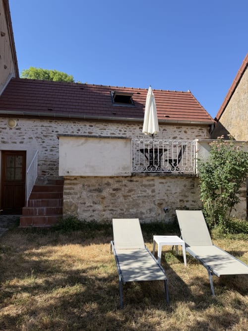 Cottage garden at Domaine les Bertrands with lounge chairs, stone walls, and umbrella under blue sky