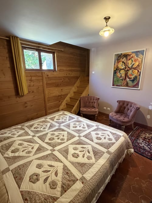 Cozy cottage bedroom at Domaine les Bertrands with patterned quilt, wooden beams, and garden view window in Couches, France