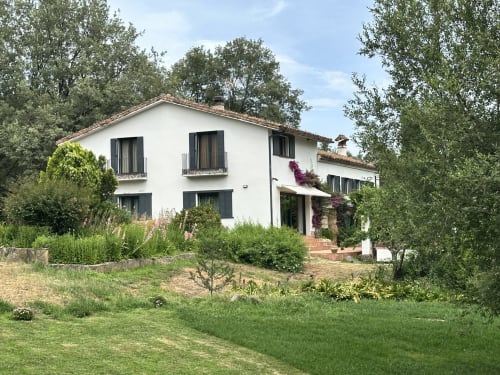El Escondite De Pedro Malillo B&B en Candeleda: casa con muros blancos, postigos negros y jardín exuberante rodeado de árboles.