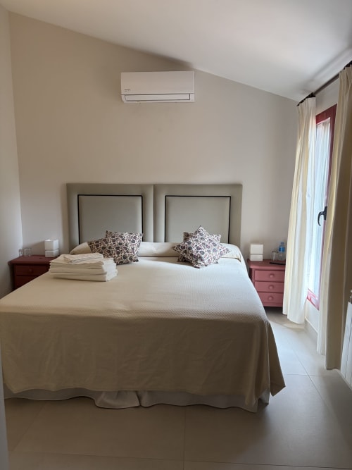 Dormitorio luminoso con ropa de cama blanca, cabeceros dobles, almohadones decorativos y aire acondicionado en El Escondite De Pedro
