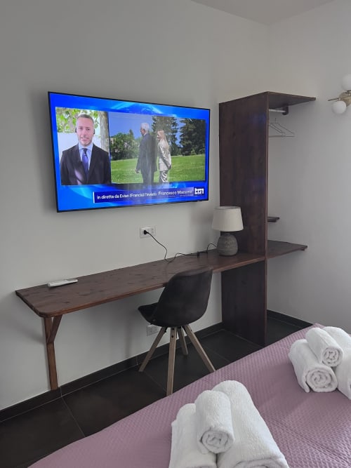 Area di lavoro in camera d'hotel con scrivania, sedia nera e TV 55" con programmi italiani a Rocca di Papa