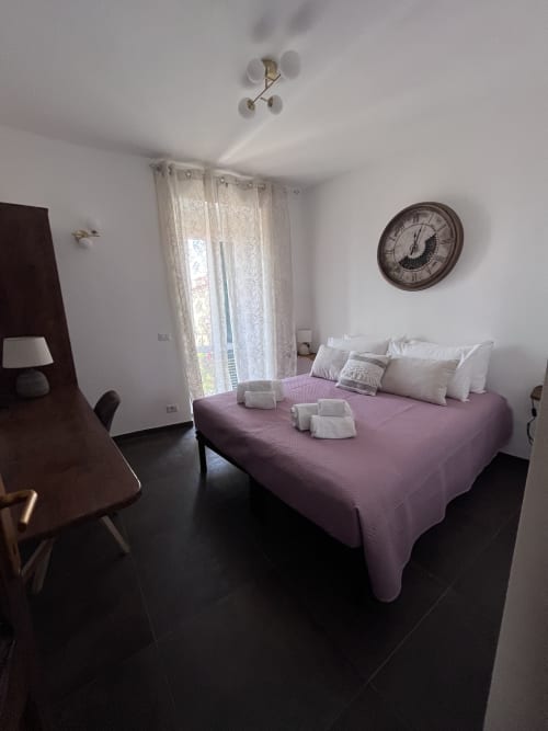Camera moderna a Cuore di Rocca a Rocca di Papa con letto viola, cuscini bianchi, pavimento scuro e orologio vintage