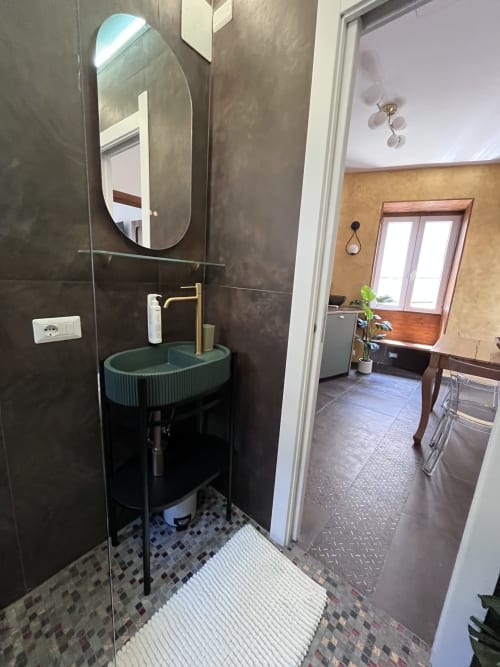 Bagno moderno a Rocca di Papa con lavabo turchese, specchio ovale, pareti in piastrelle scure e box doccia in vetro