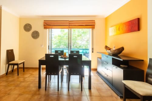 Comedor moderno en apartamento Marina Galé, Portimão con paredes amarillas, mesa de comedor negra y vistas al océano desde el balcón