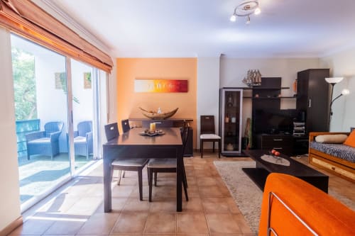 Sala de estar moderna con comedor, pared acentuada en naranja, muebles negros y vistas al balcón en Portimão
