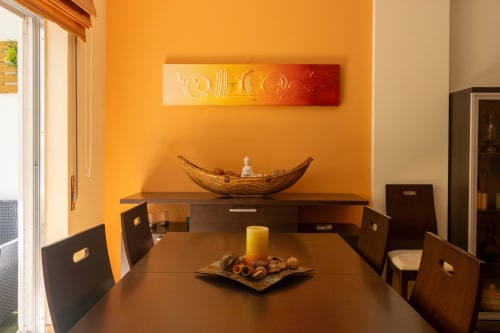 Área de comedor moderno con pared acentuada en naranja, mesa y sillas de madera oscura, escultura decorativa de barco y vela amarilla en Urban