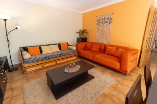 Luminosa sala de estar del Apartamento Marina Galé en Portimão con sofá naranja, cama nido con rayas de cebra y mobiliario moderno