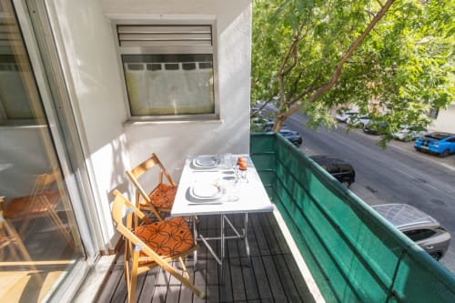 Balcón soleado en Urban Beach Rentals de Portimão con zona de comedor, sillas amarillas y vista a la calle con coches aparcados