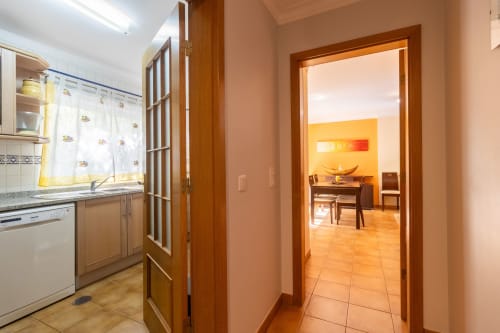 Moderna cocina y comedor en apartamento de Portimão con puertas de madera, electrodomésticos blancos y tonos terracota cálidos