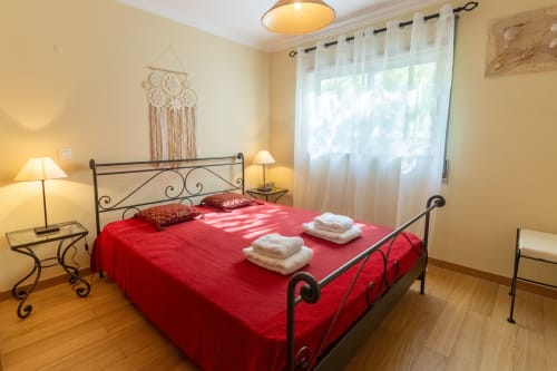 Dormitorio luminoso con ropa de cama roja, cama de hierro forjado y vistas a la ciudad en Urban Beach Rentals en Portimão