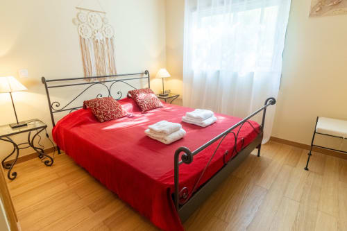 Dormitorio luminoso con ropa de cama roja, cama de hierro forjado negro, toallas blancas y vistas a la ciudad en Urban Beach Rentals Portimão