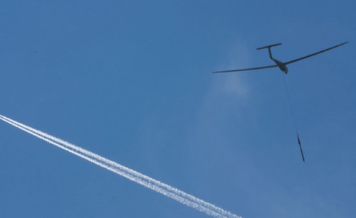 Glider and aircraft with contrails soaring above La Roche Guyon near Giverny