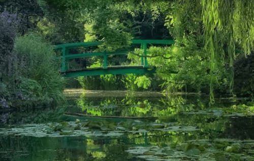 Green arched bridge over tranquil pond with lush garden foliage, Le Paradis de Lucile near Giverny