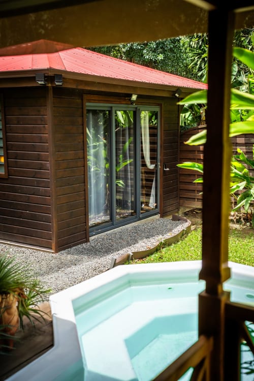 Cottage West Indies La Trace du Contrebandier : chalet en bois avec toit rouge, bain à remous en avant-plan, jardin tropical
