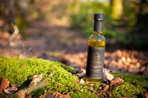 Bouteille d'huile d'olive Ô Cèpes exposée sur un sol couvert de mousse au Domaine de Châlus-Chabrol, un gîte français à Châlus.