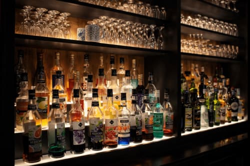 Comptoir de bar illuminé avec bouteilles de spiritueux et verrerie au restaurant Auberge La Source Bleue, Cusance