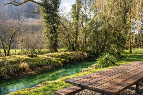 Terrasse en bois surplombant un ruisseau turquoise avec des saules pleureurs à l'Auberge La Source Bleue à Cusance, France