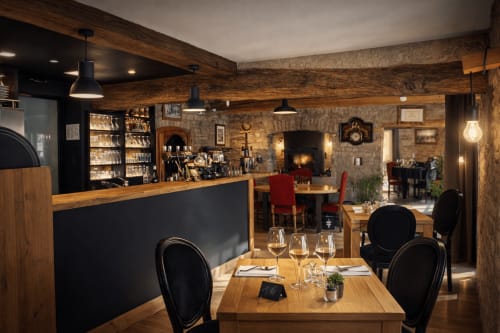 Salle à manger élégante de l'Auberge Restaurant La Source Bleue à Cusance avec poutres en bois, cheminée et bar à vins.