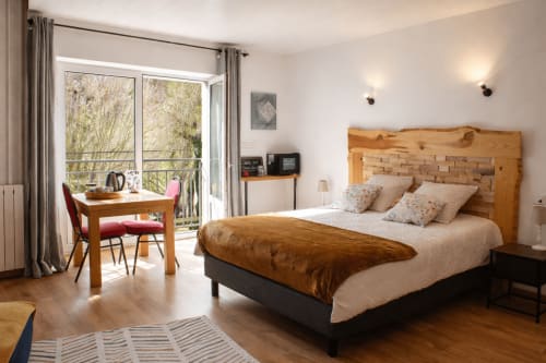 Chambre lumineuse à La Source Verte à Cusance avec lit en bois, balcon vue sur jardin, bureau et parquet