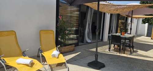 Terrasse ensoleillée de Mi Casa Es Su Casa avec transats jaunes, table à manger, voiles d'ombrage et entrée moderne de l'appartement