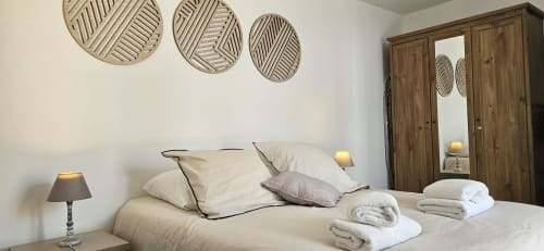 Chambre Le Loft avec literie crème, armoire en bois, paniers muraux décorés et lampes de chevet chez Mi Casa Es Su Casa