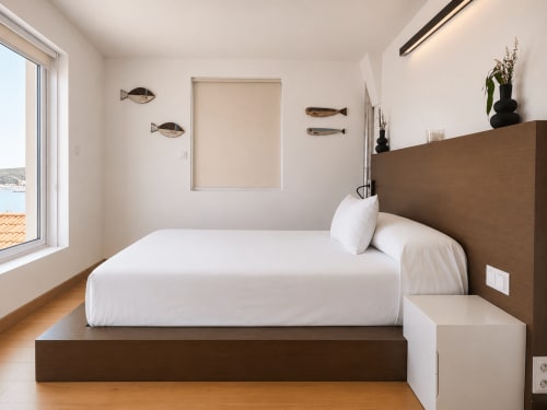 Habitación moderna del apartamento Holibai en Nigrán con vistas al mar, cabecero marrón, ropa de cama blanca, suelo de madera y decoración náutica