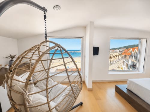 Moderno apartamento frente al mar en Nigrán con silla colgante de ratán, suelos de madera y terraza con vistas al mar y a Playa América