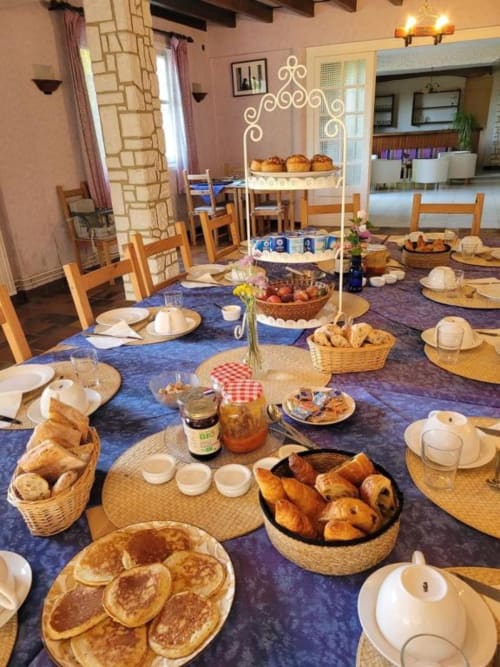 Buffet du petit-déjeuner à la Domaine de la Gare M à Mortagne-sur-Gironde avec viennoiseries, paniers de pain et couverts