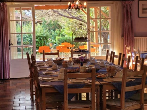 Élégante salle à manger du Domaine de la Gare avec table ronde, chaises en bois et vue sur le jardin par les portes-fenêtres.