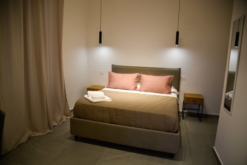 Camera da letto moderna presso l'Onde Del Mare B&B a Napoli con letto verde oliva, cuscini rosa, lampade a sospensione e pavimento in piastrelle