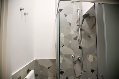 Moderna cabina doccia con piastrelle geometriche in bagno hotel napoletano, dotata di rubinetteria cromata e soffione pioggia