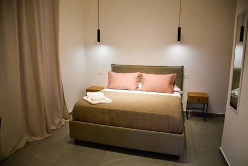 Camera da letto moderna all'Onde Del Mare di Napoli con letto verde oliva, cuscini rosa, illuminazione a sospensione e pavimento piastrellato
