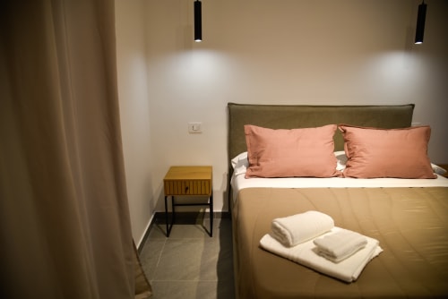 Camera da letto matrimoniale moderna a Onde Del Mare B&B a Napoli con testiera in ulivo, cuscini corallo e illuminazione contemporanea