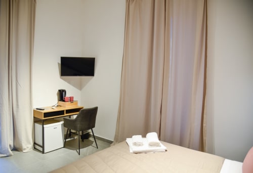 Camera doppia moderna presso Onde Del Mare B&B a Napoli con letto, scrivania, TV a parete e tende con vista sul giardino