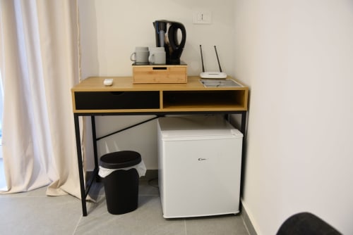 Angolo studio compatto con scrivania in legno, mini frigo, bollitore elettrico e router Wi-Fi nella camera B&B a Napoli